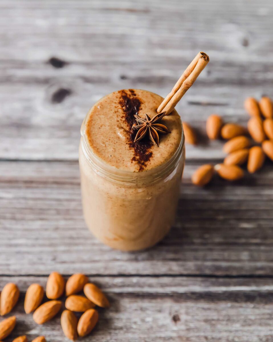A mason jar is filled with freshly made cinnamon spiced almond butter, and is garnished with cinnamon and a star anise.