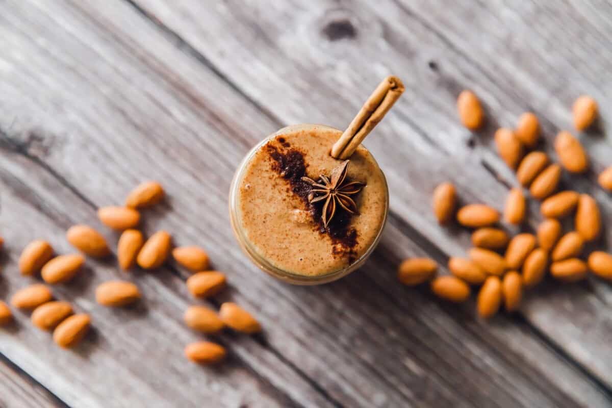 A jar of cinnamon almond butter is presented on a wooden surface and is surrounded by almonds. 