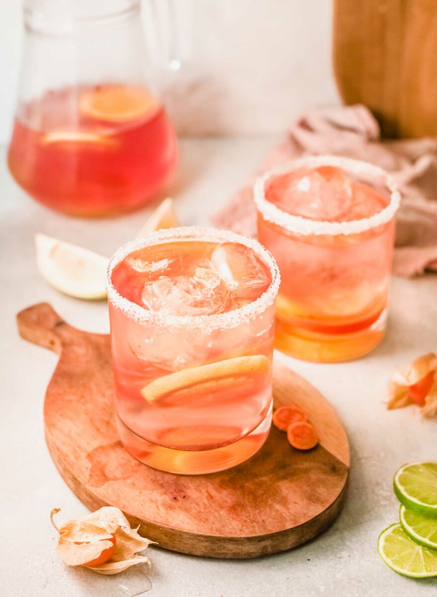 Two glasses of pink sangria are placed next to a full pitcher. 