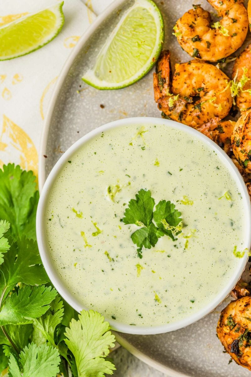 Grilled shrimp are placed next to a bowl of creamy cilantro dressing. 