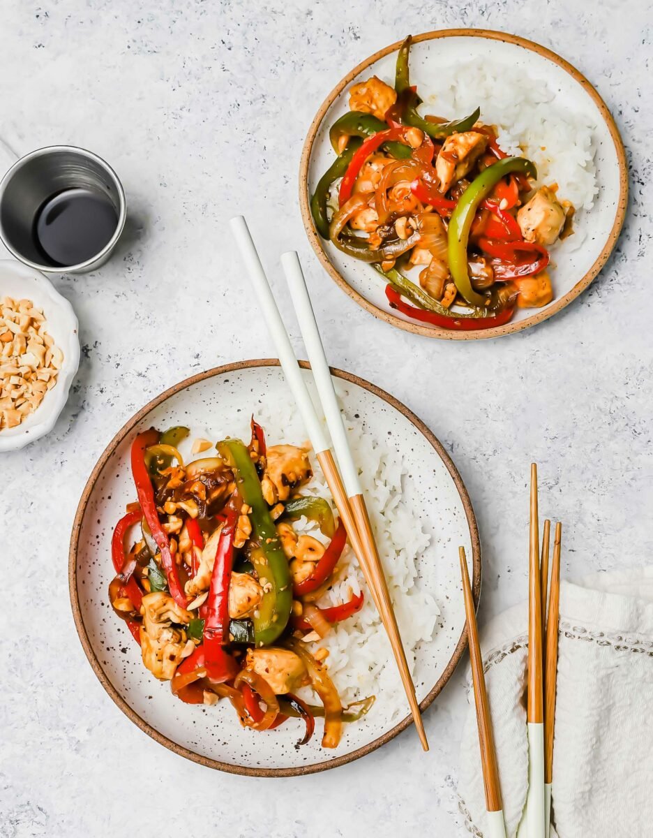 Two servings of rice and Kung Pao chicken are placed on a white countertop next to chopsticks and a small bowl of soy sauce.