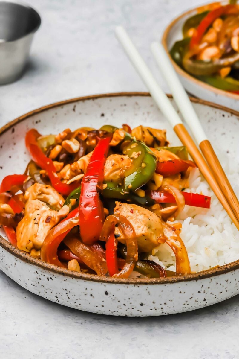 A small bowl of white rice and Kung Pao chicken is ready to be eaten with chopsticks. 