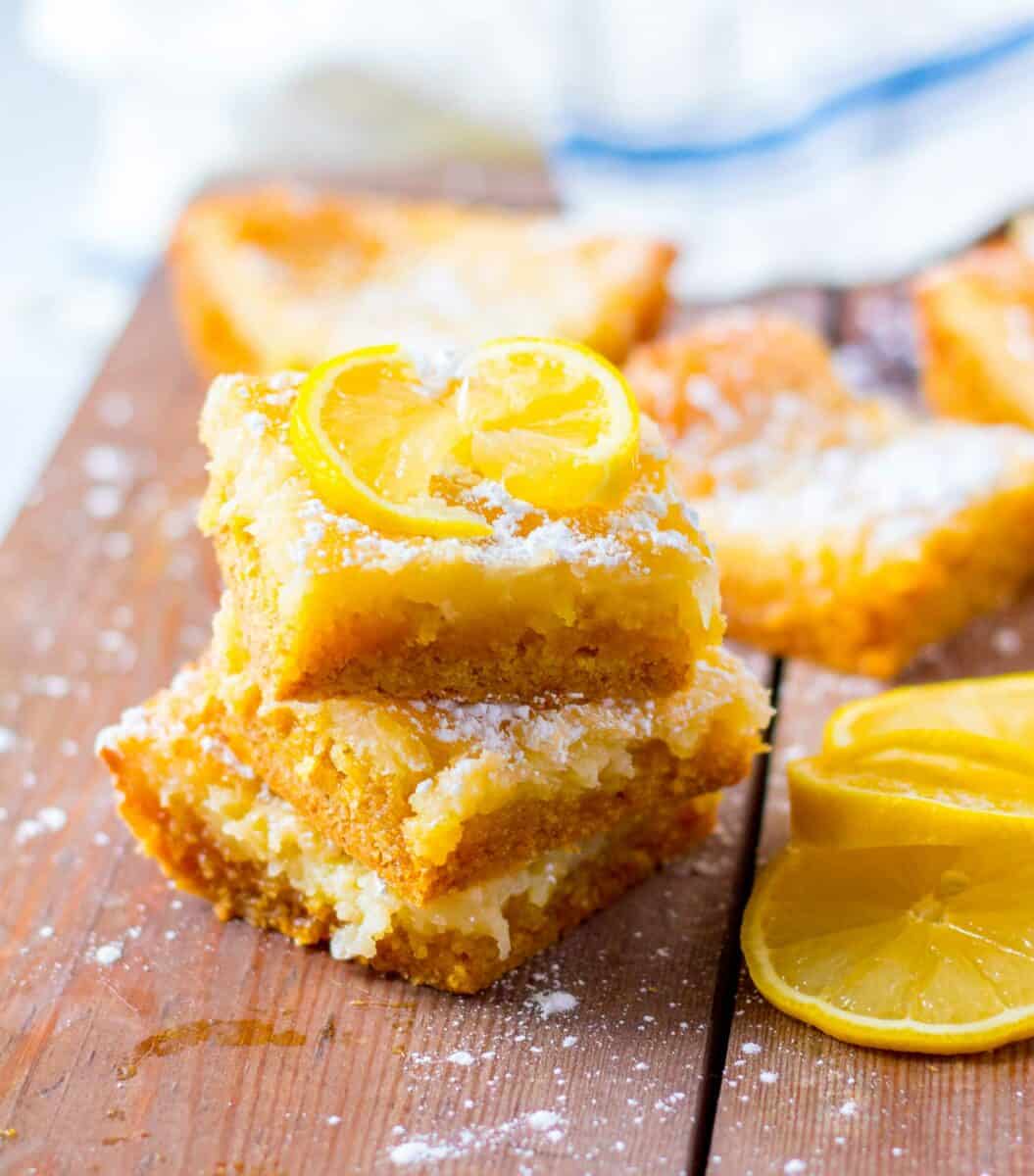 A few pieces of lemon cake are stacked on top of one another on a wooden surface. 