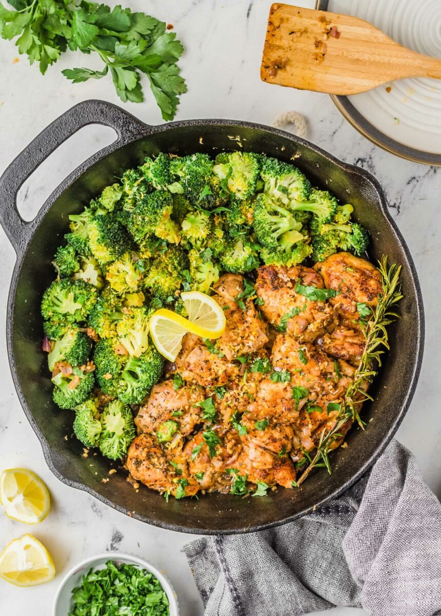 A lemon is twisted in the middle of a broccoli and chicken skillet. 