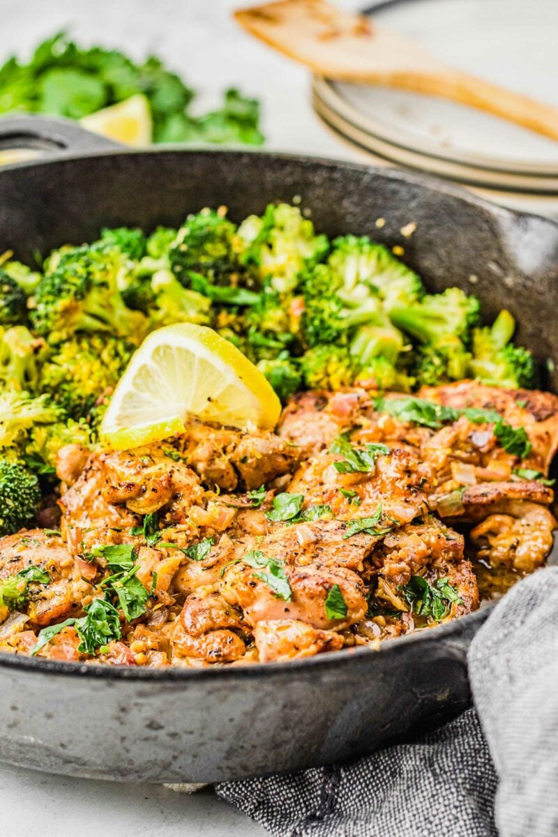 Lemon garlic chicken thighs in a skillet are garnished with fresh parsley. 