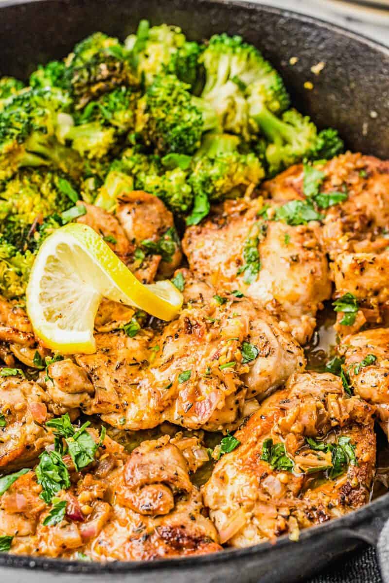 Fully cooked lemon garlic chicken thighs are in a skillet next to cooked broccoli.