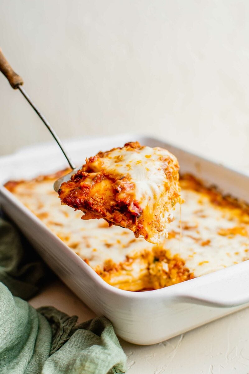 A spatula is lifting a piece of ravioli lasagna out of the baking dish.