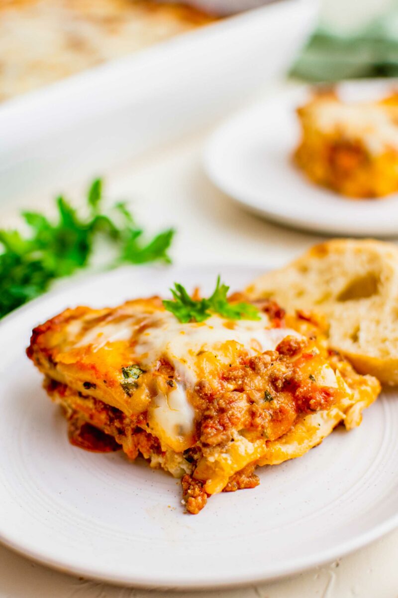 Cheesy, meaty lasagna is garnished with parsley on a white plate.