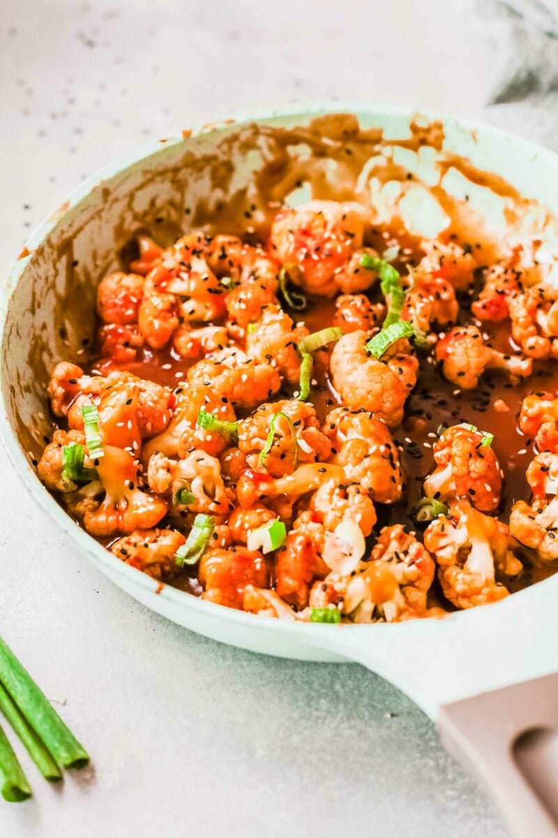 A white skillet contains a large portion of sticky orange cauliflower. 