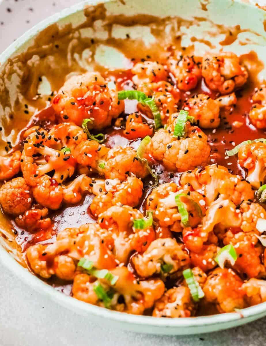 Chopped green onions and black sesame seeds garnish a skillet full of cauliflower.