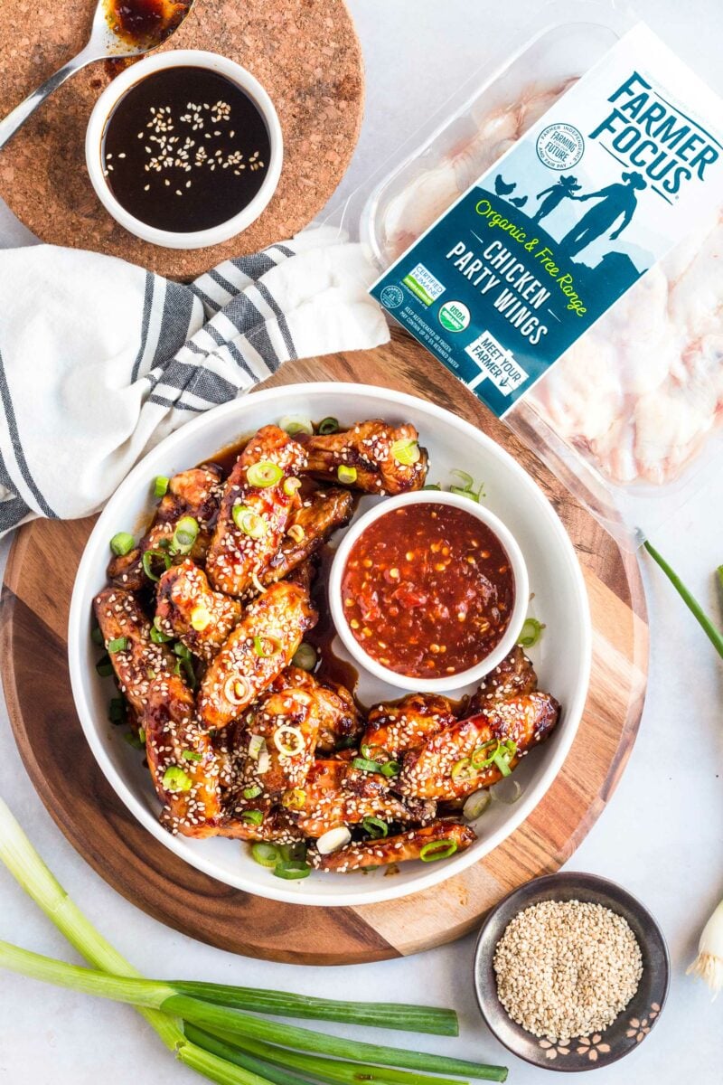 A bowl of ready to eat chicken wings is placed next to an unopened container of Farmer Focus chicken party wings. 