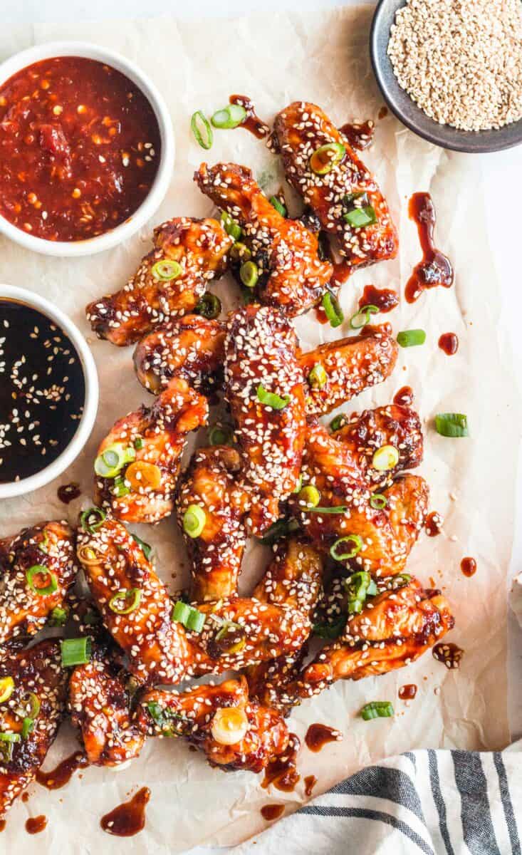 Multiple sticky chicken wings are spread out on a sheet of brown parchment paper. 