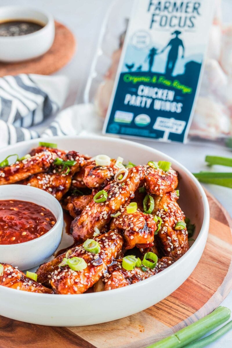 Chicken wings are garnished with sesame seeds and chopped green onions in a medium sized white serving bowl. 