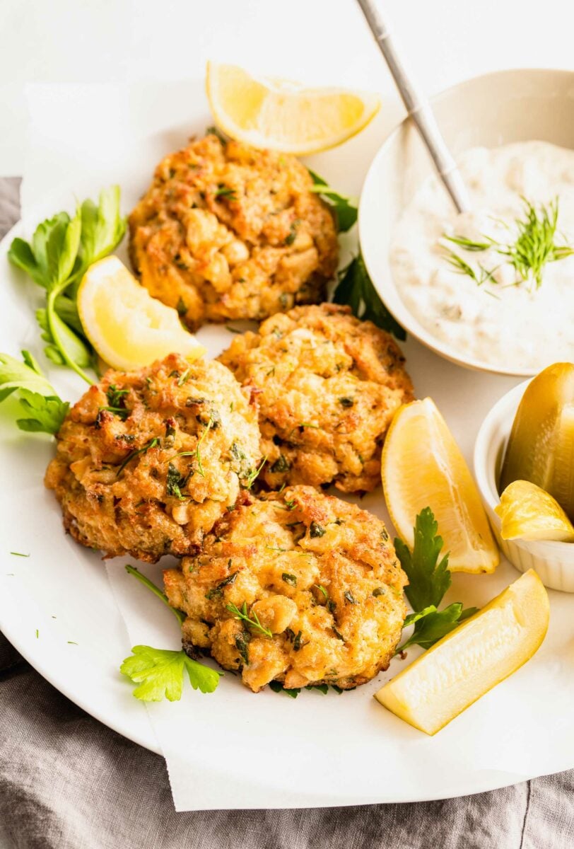 Tartar sauce is placed next to pickle spears and crab cakes. 