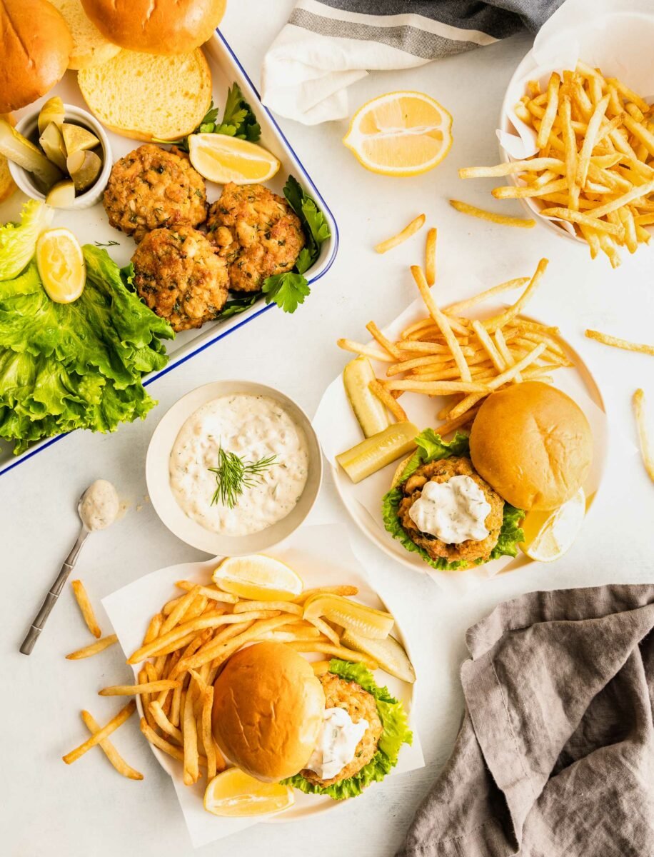 Two plates contain crab cake sandwiches and French fries. 