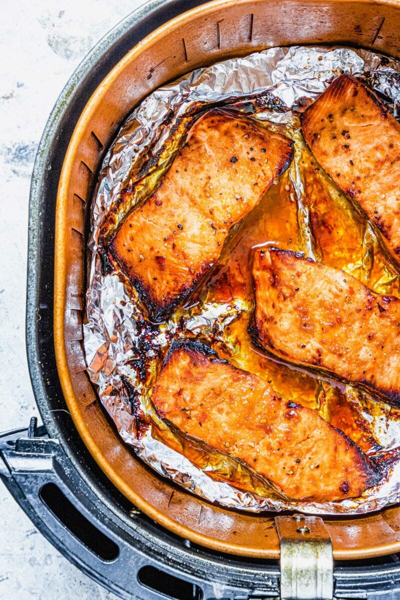 Four salmon fillets are in the basket of an air fryer. 