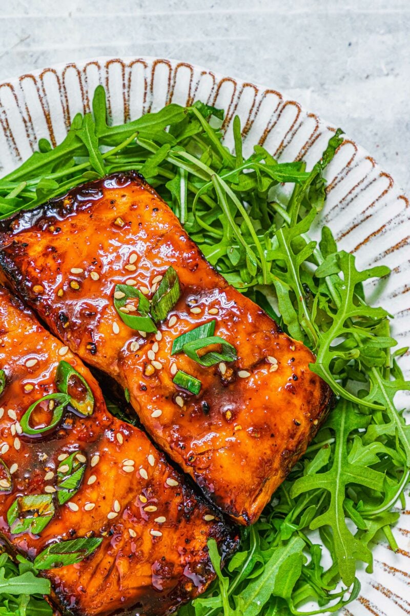 Fresh greens and salmon are on a white plate. 