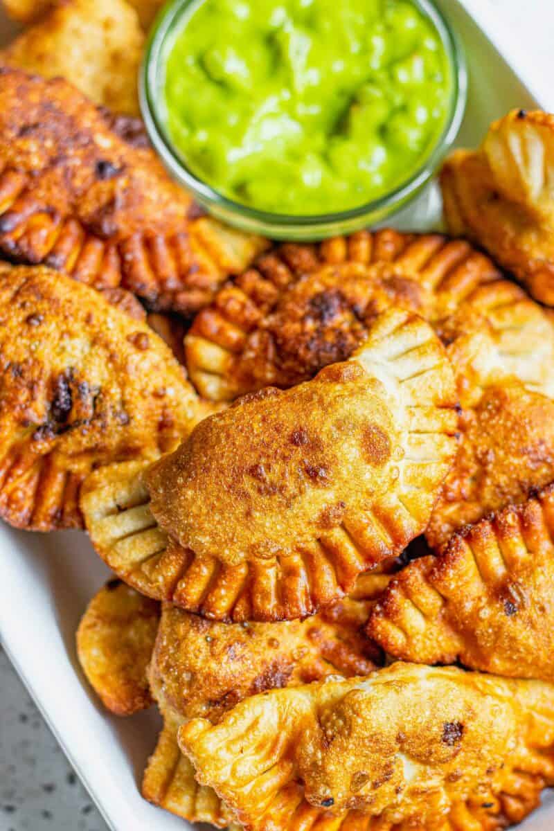 Several empanadas are placed next to a small glass bowl filled with dipping sauce. 