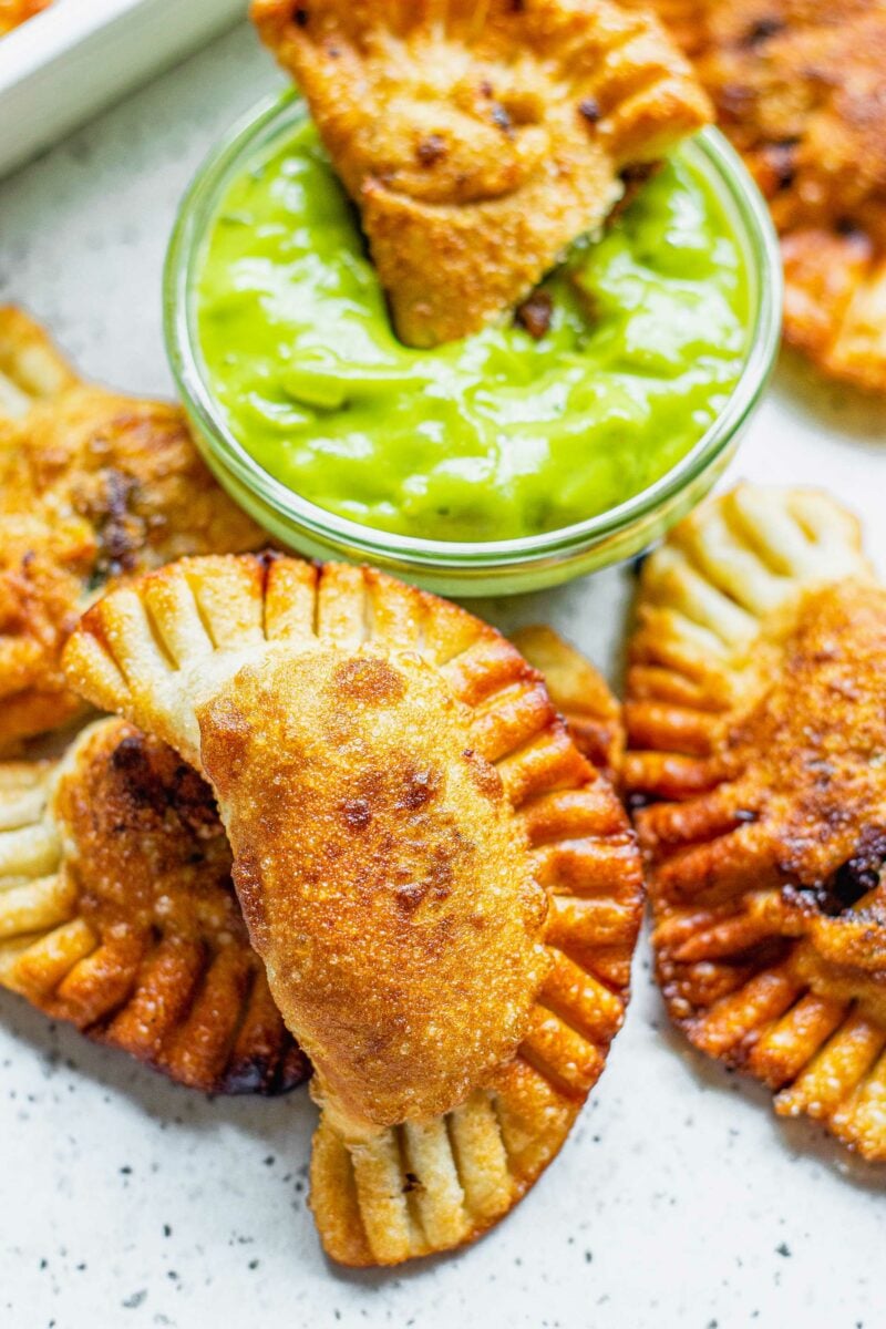 An empanada is being dipped into green sauce. 