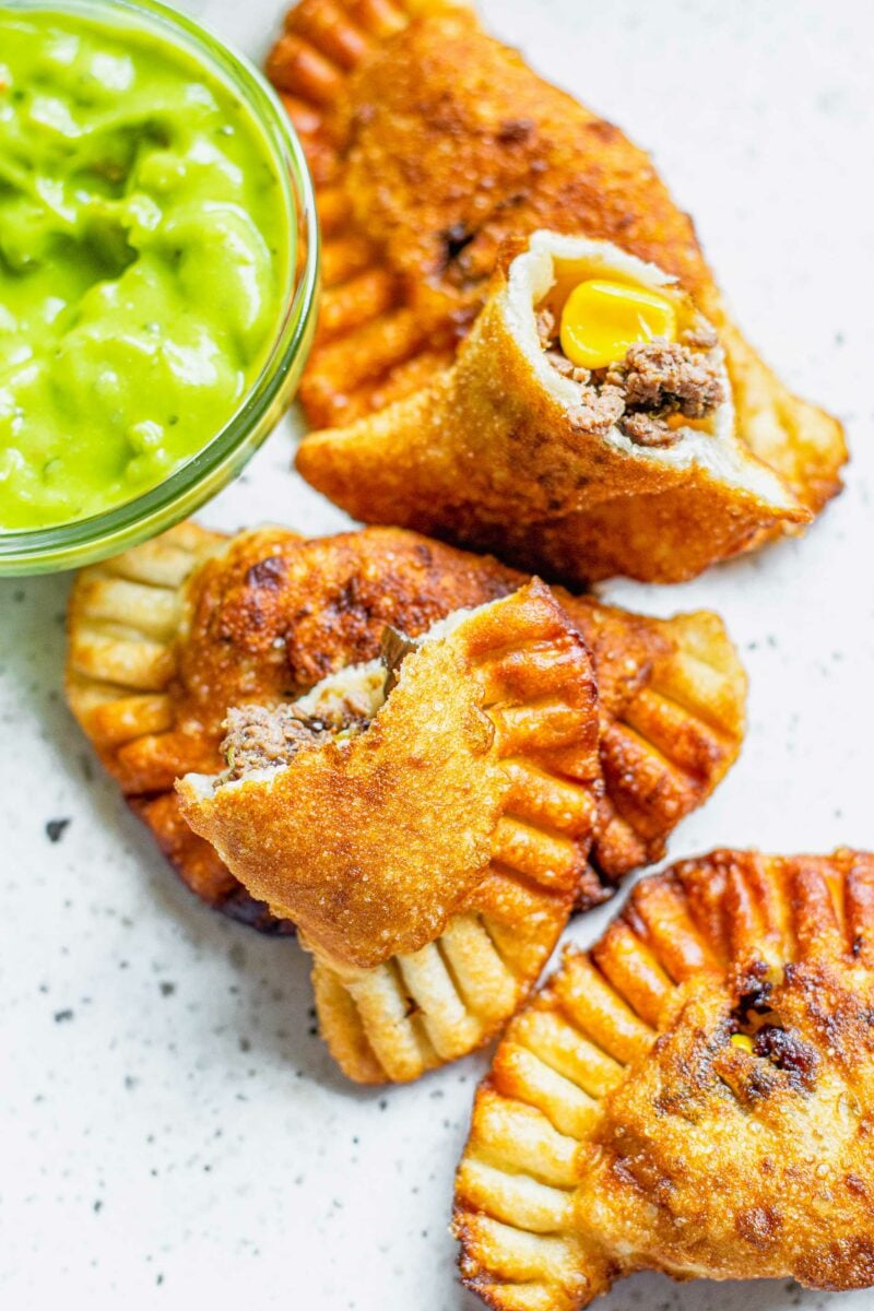 One empanada has been split in half next to several whole empanadas. 