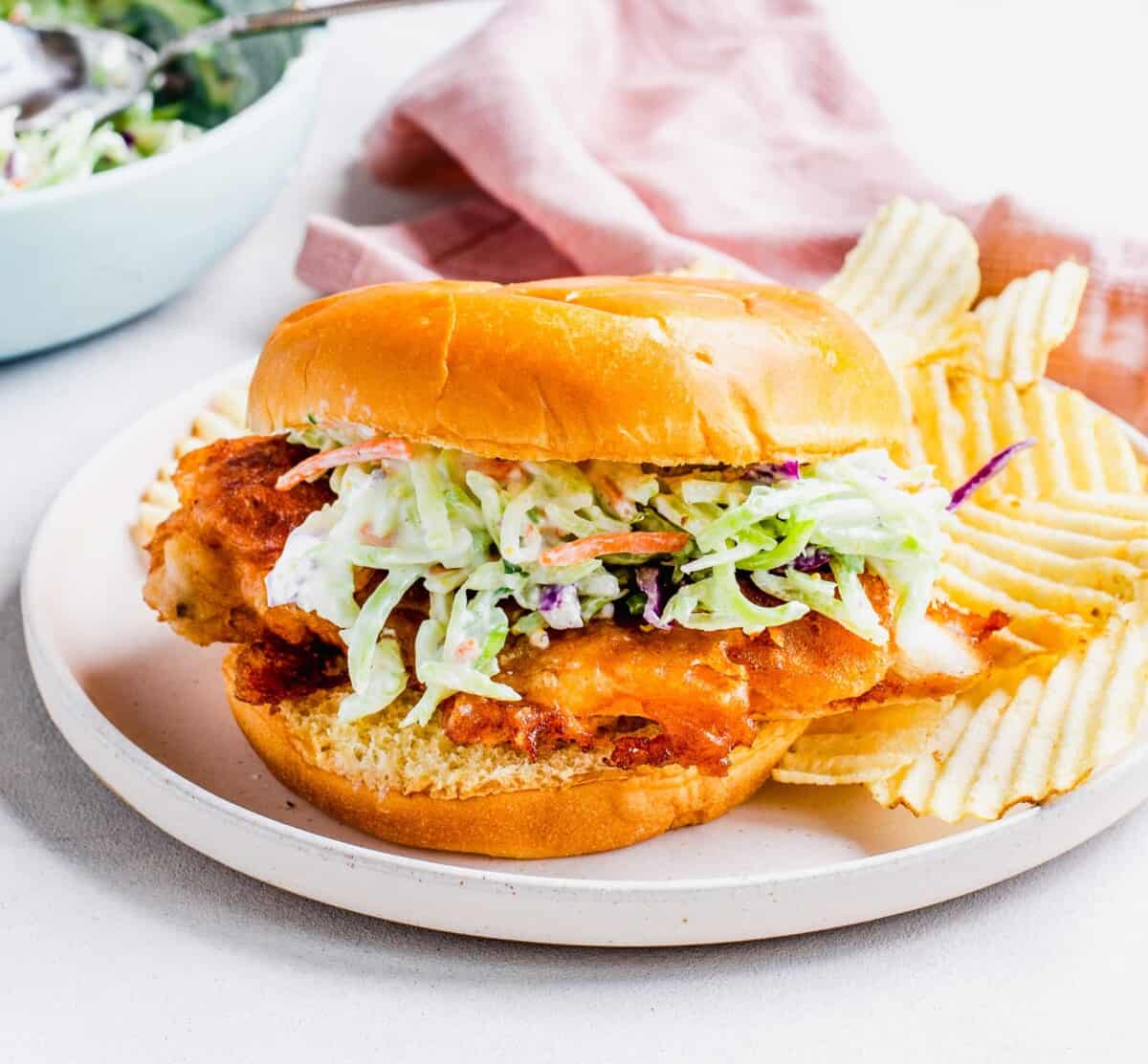 Potato chips are placed next to a chicken sandwich.