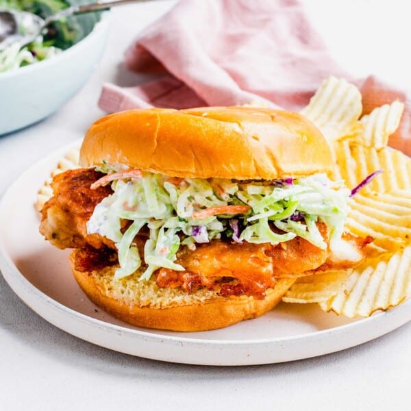 Potato chips are placed next to a chicken sandwich.