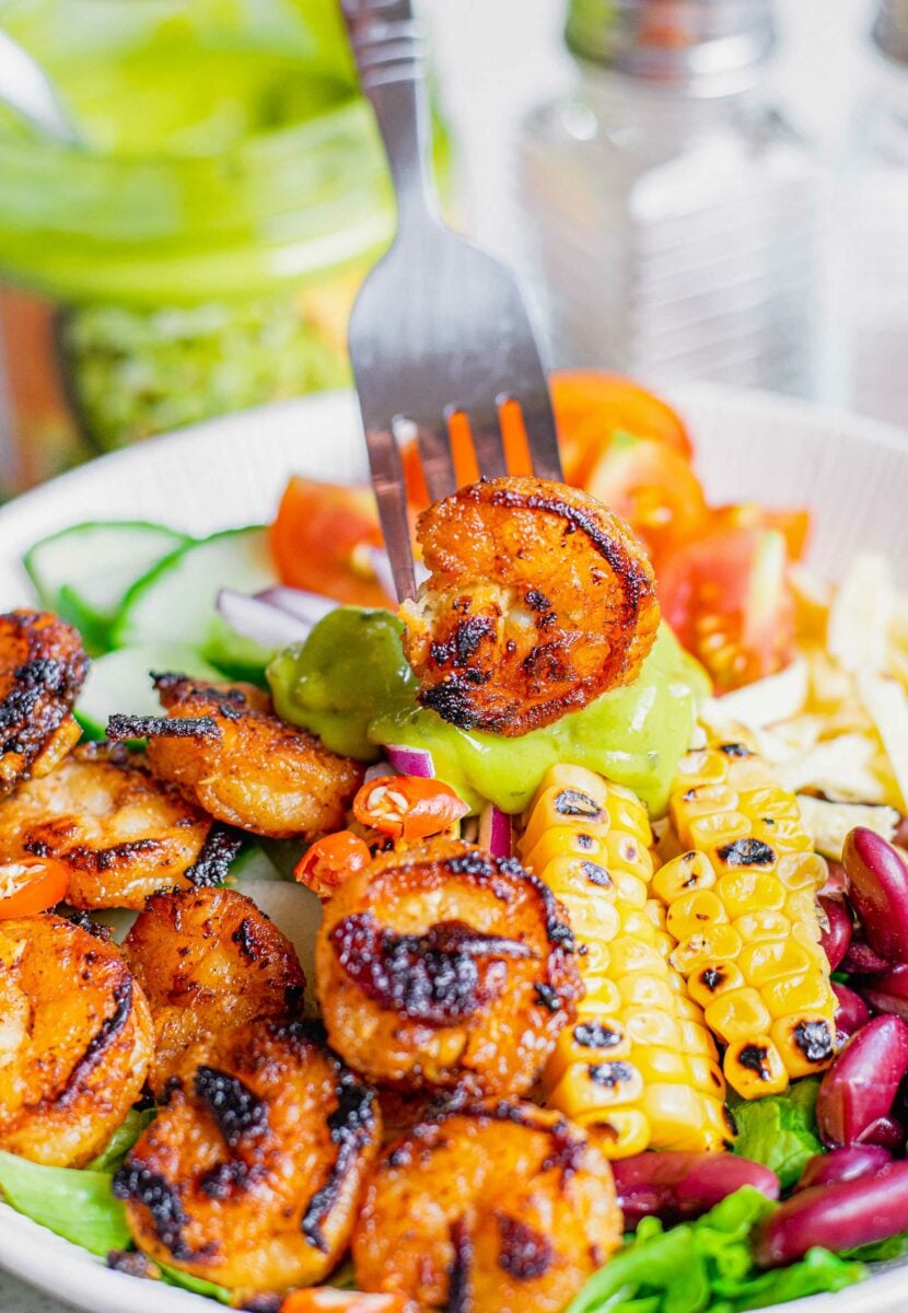 A blackened shrimp is being lifted from the bowl with a fork. 