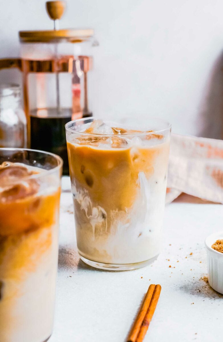 A cinnamon stick is placed next to two full glasses. 