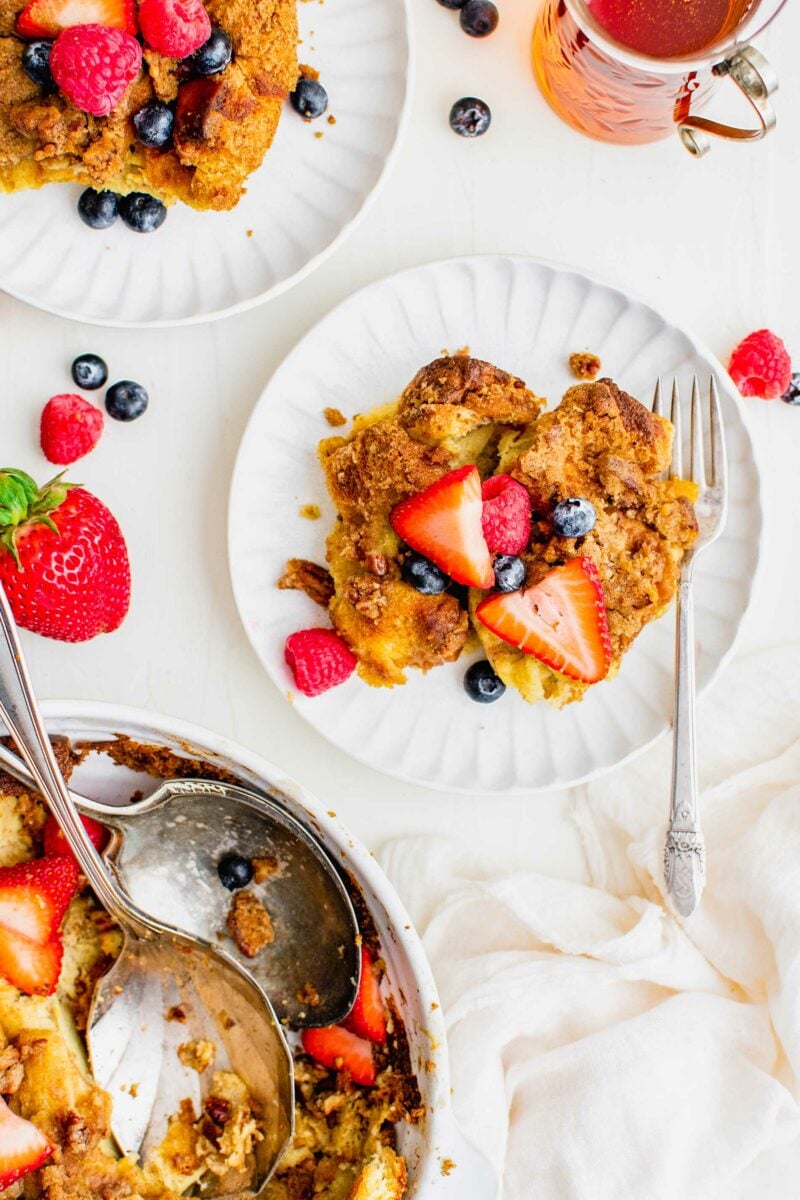 A serving of French toast casserole is on a white plate and garnished with berries. 