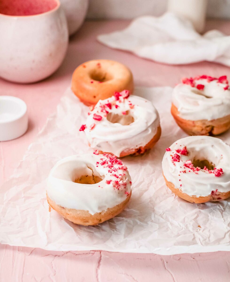 Four donuts are glazed and garnished with raspberries, while one is plain. 