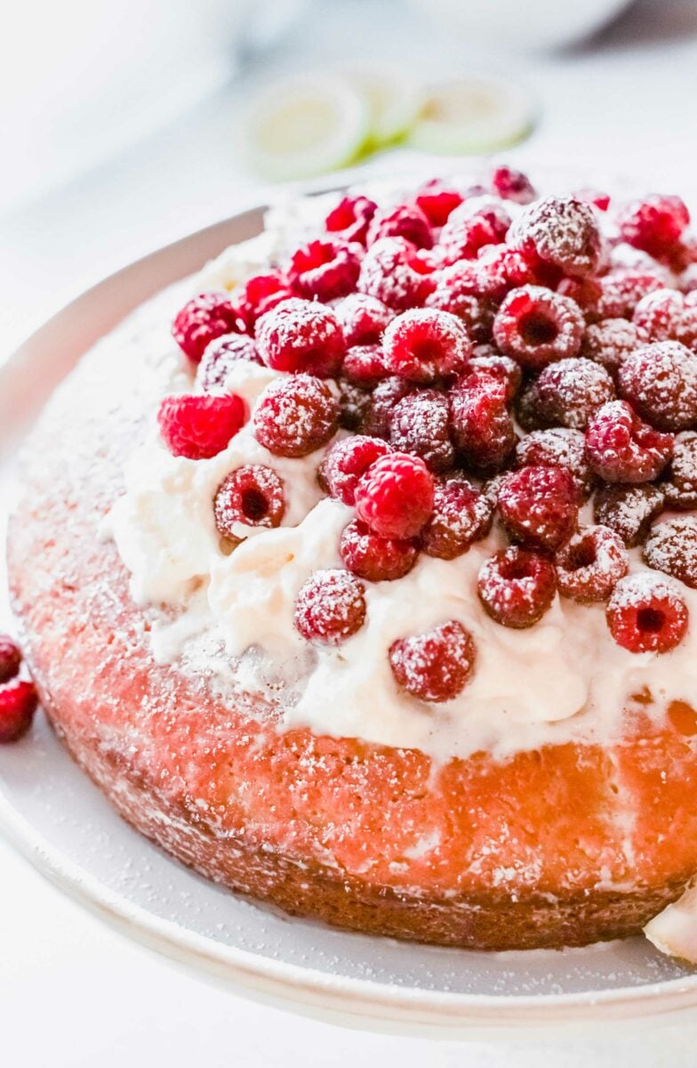 Pink raspberry cake is topped with whipped cream and berries. 