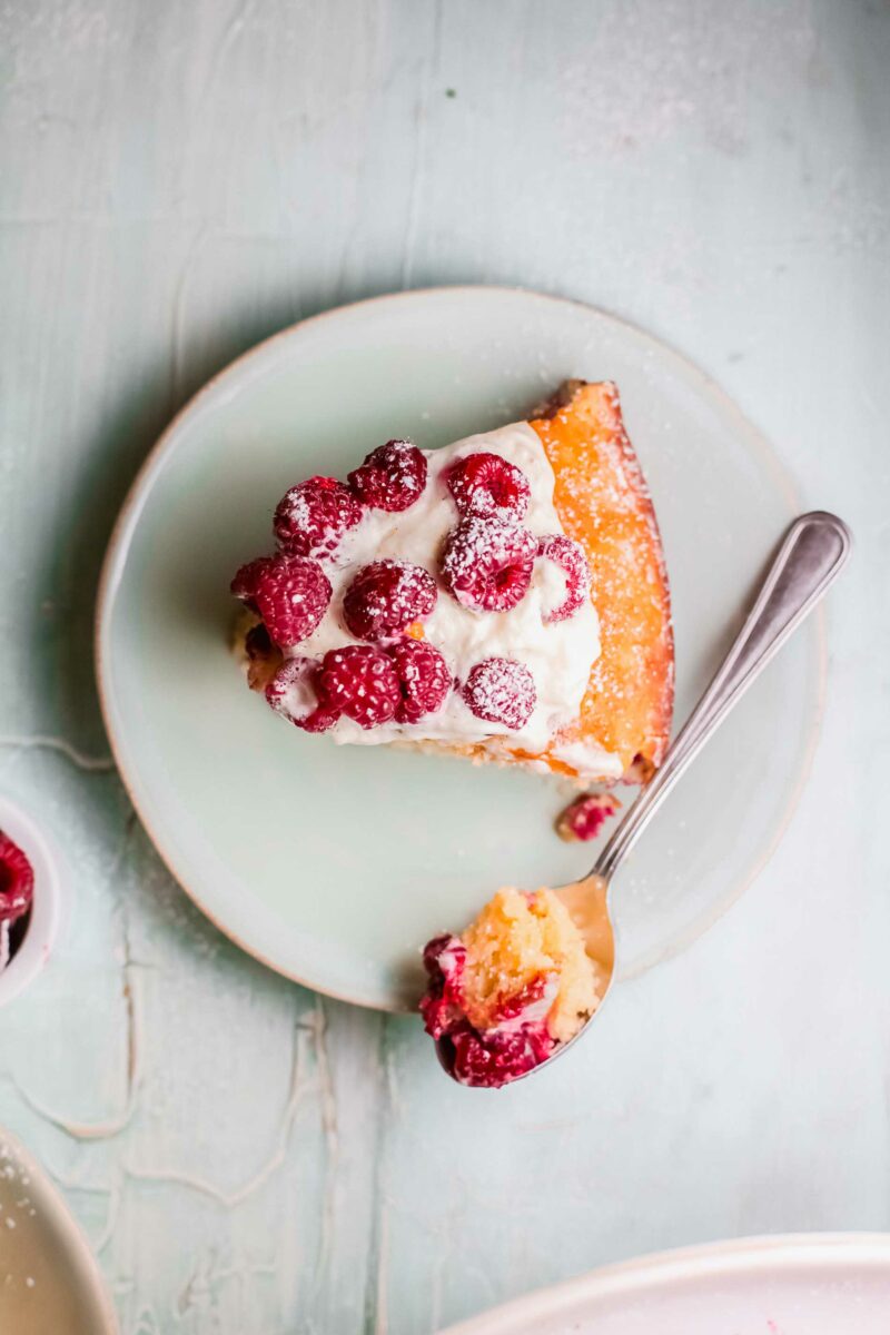 A spoon has removed a bite of raspberry cake from a piece. 