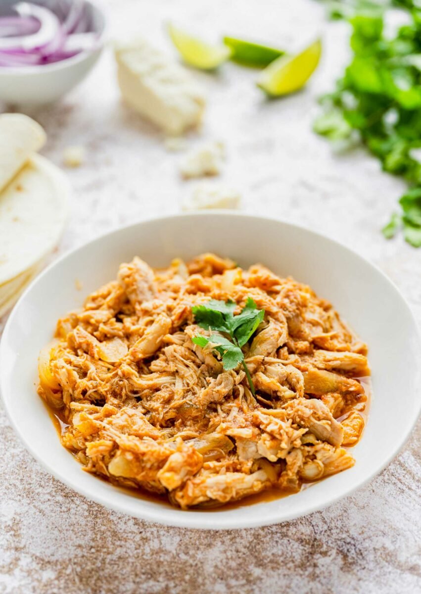 A white bowl is filled with chicken tinga meat. 