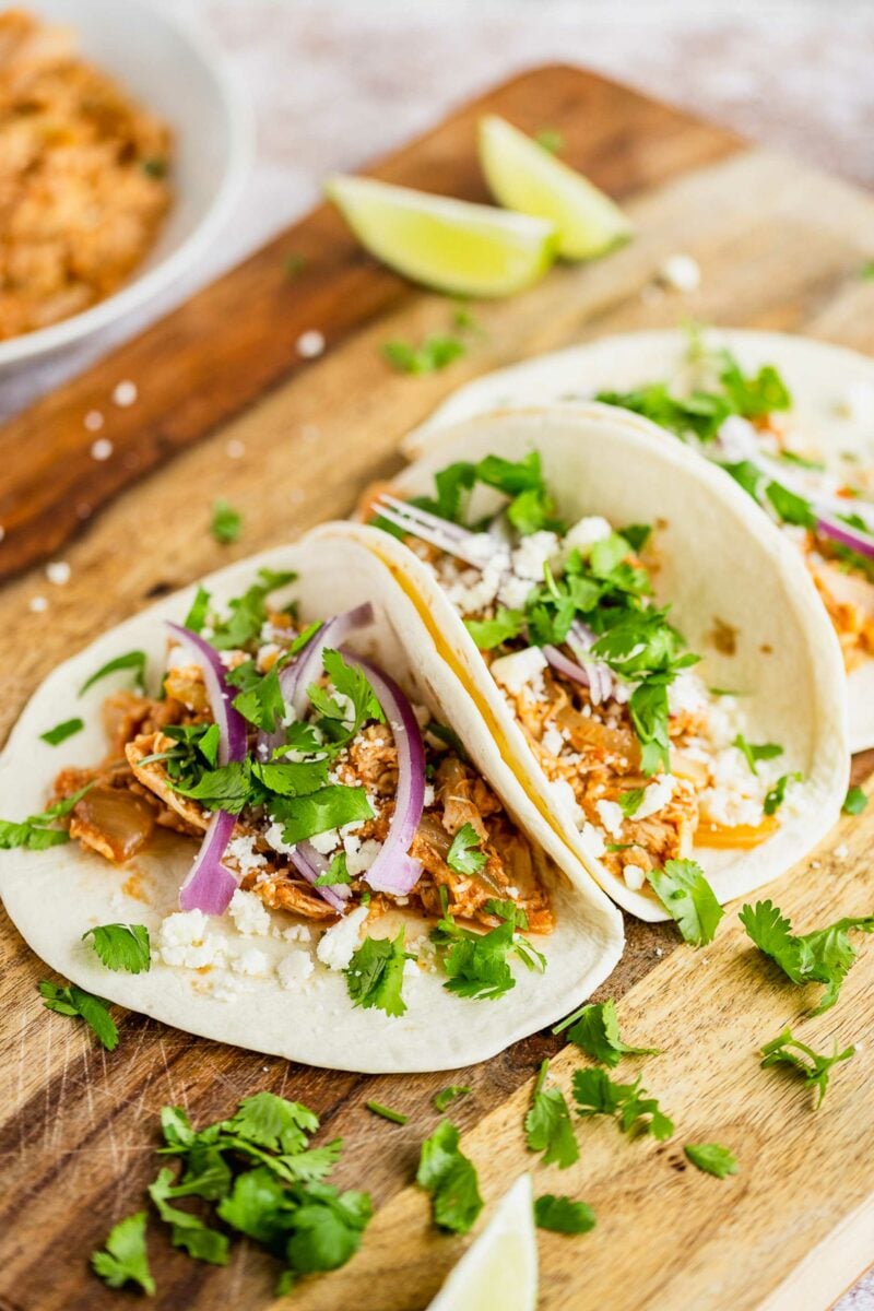 A taco is filled with cheese, chicken, onions and cilantro. 