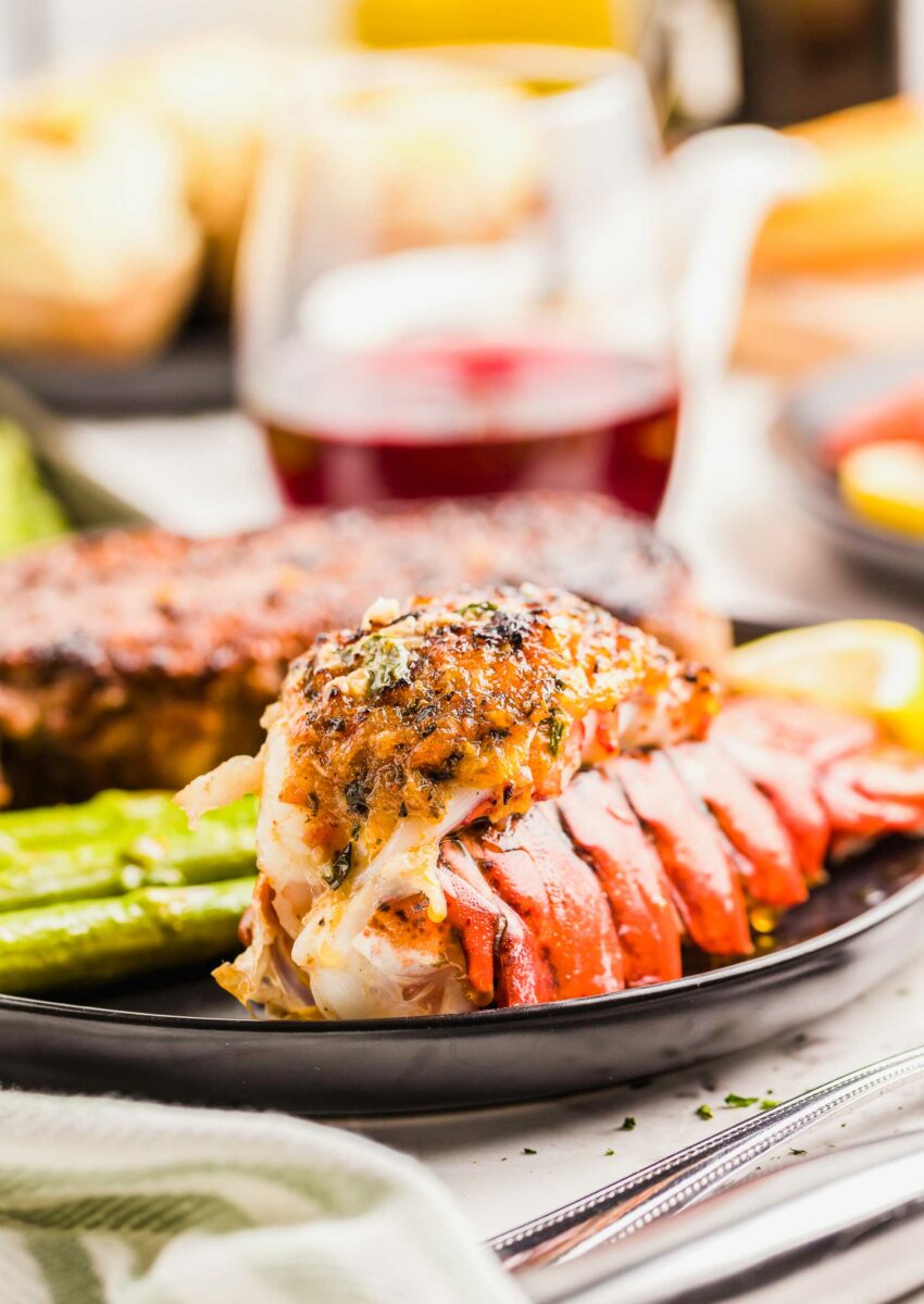 A lobster tail is fully cooked on a black plate. 