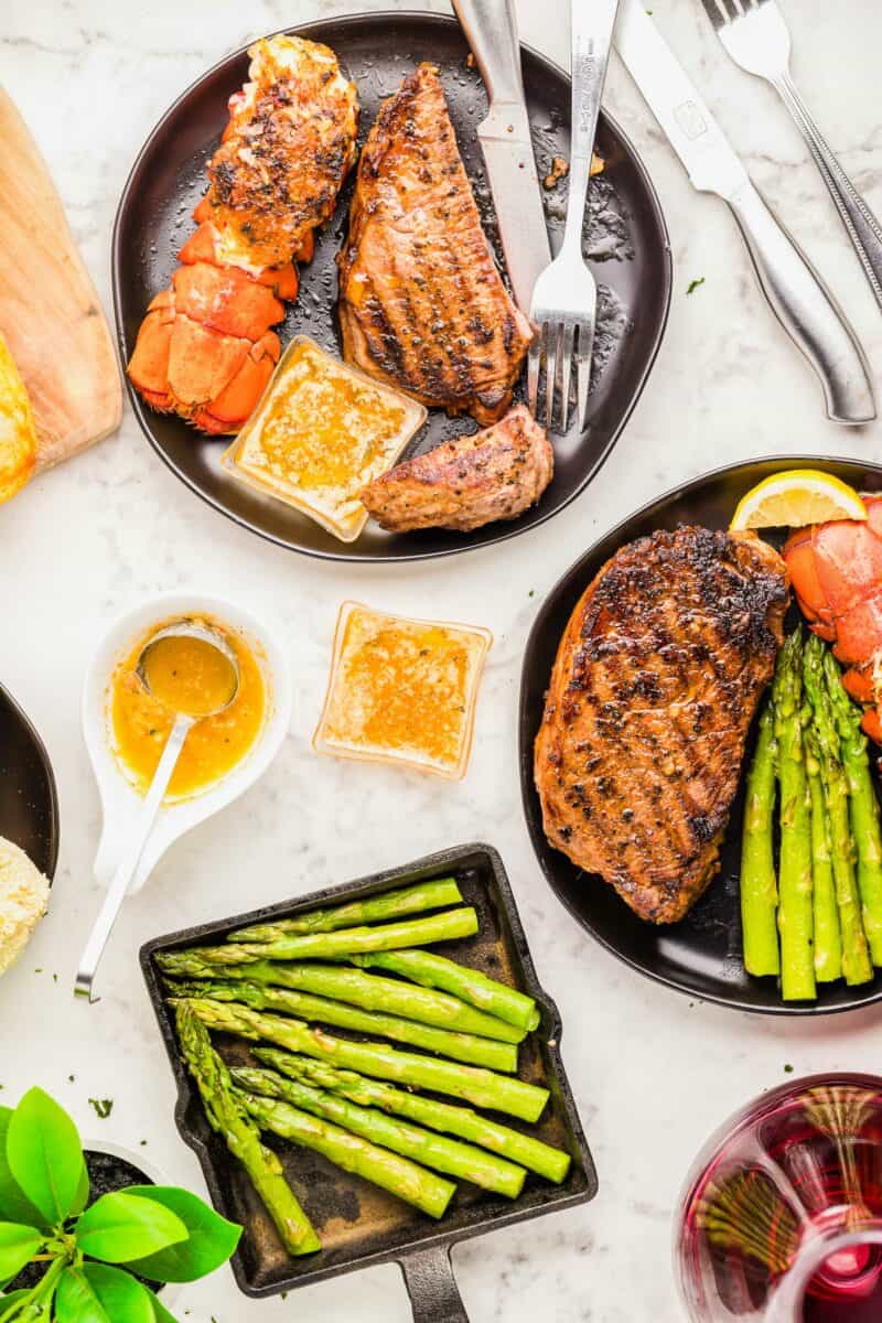 Asparagus is plated next to two plates of surf and turf. 