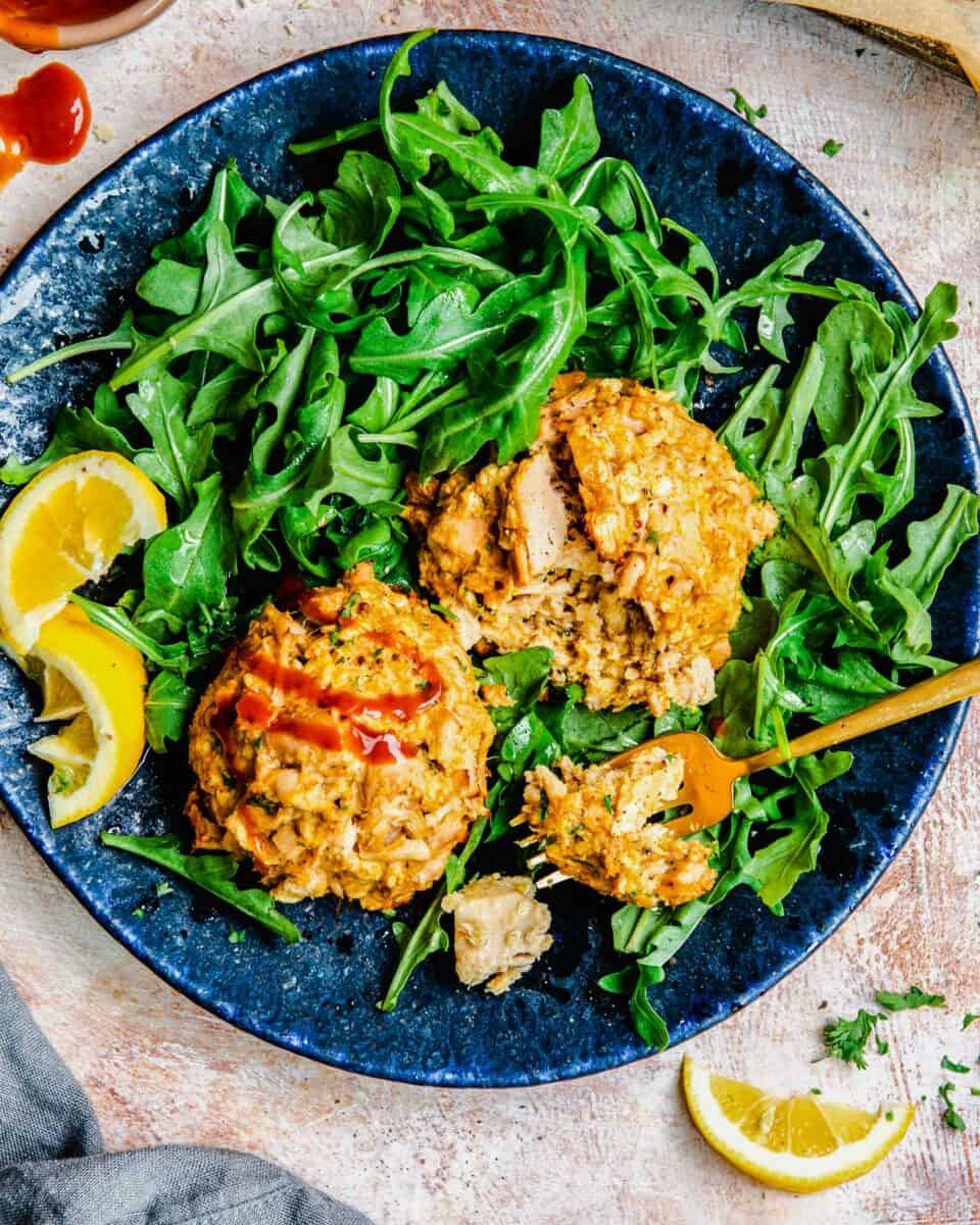 Two tuna cakes are placed on top of arugula on a blue plate.