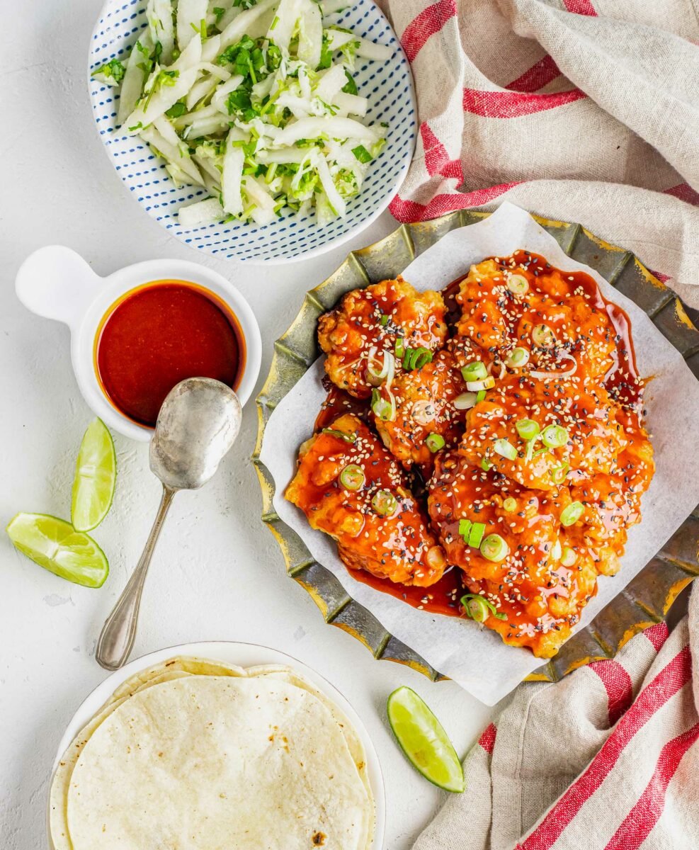 Chicken, tortillas, slaw, and extra sauce are all placed on a table. 