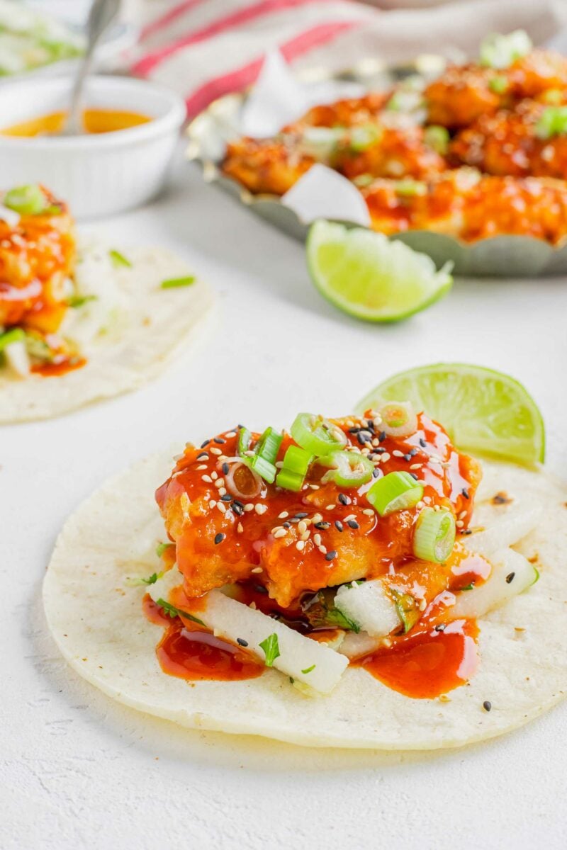 A piece of chicken is placed on top of pear slaw and a tortilla