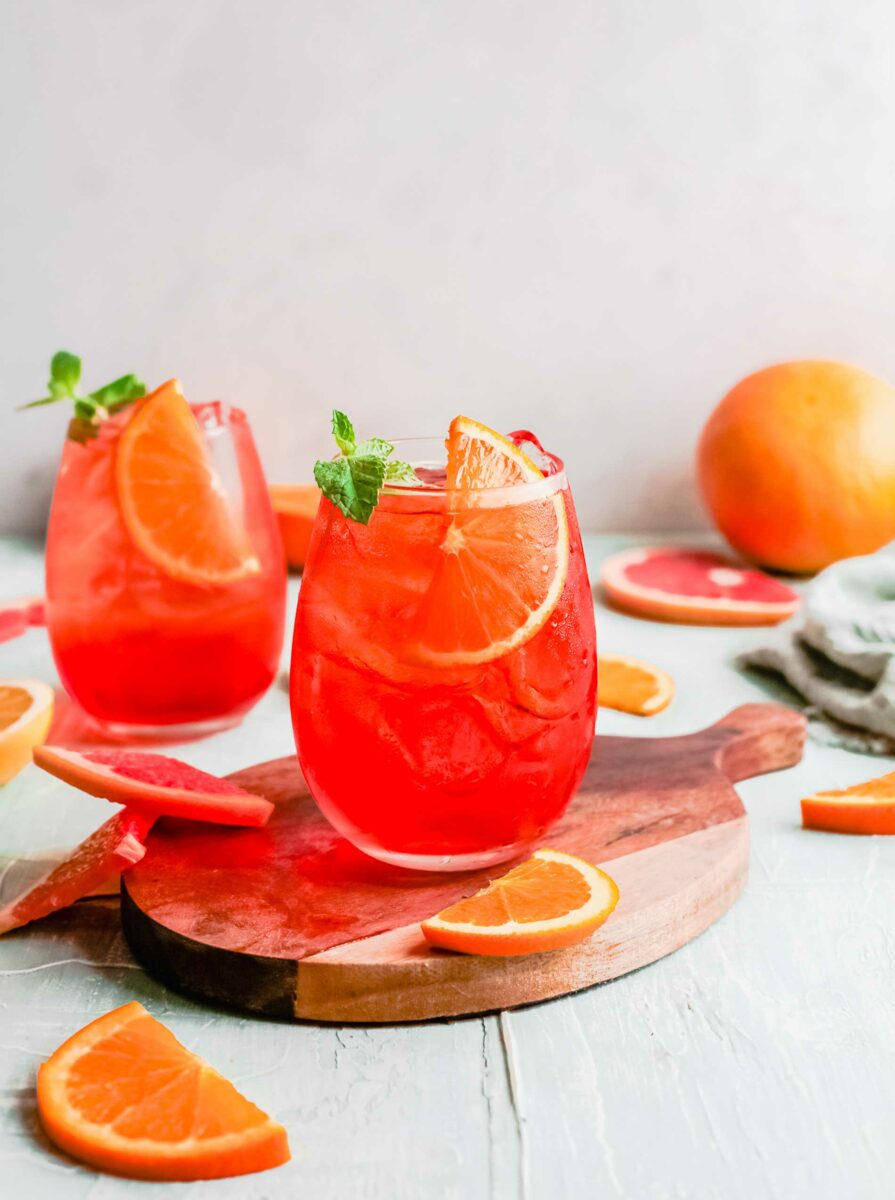 Two aperol spitzes are placed next to several orange slices. 