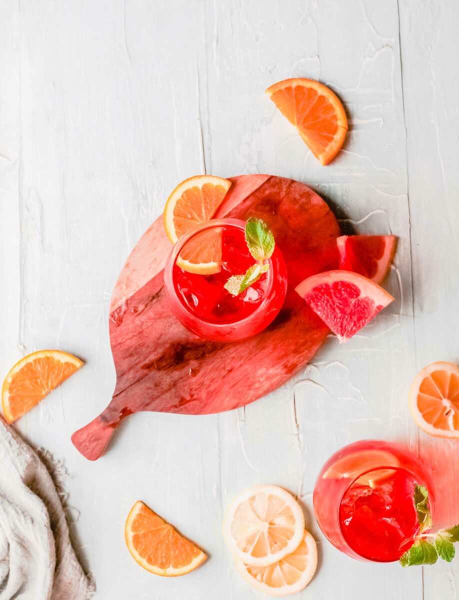 An aperol spritz is placed on a round wooden cutting board. 