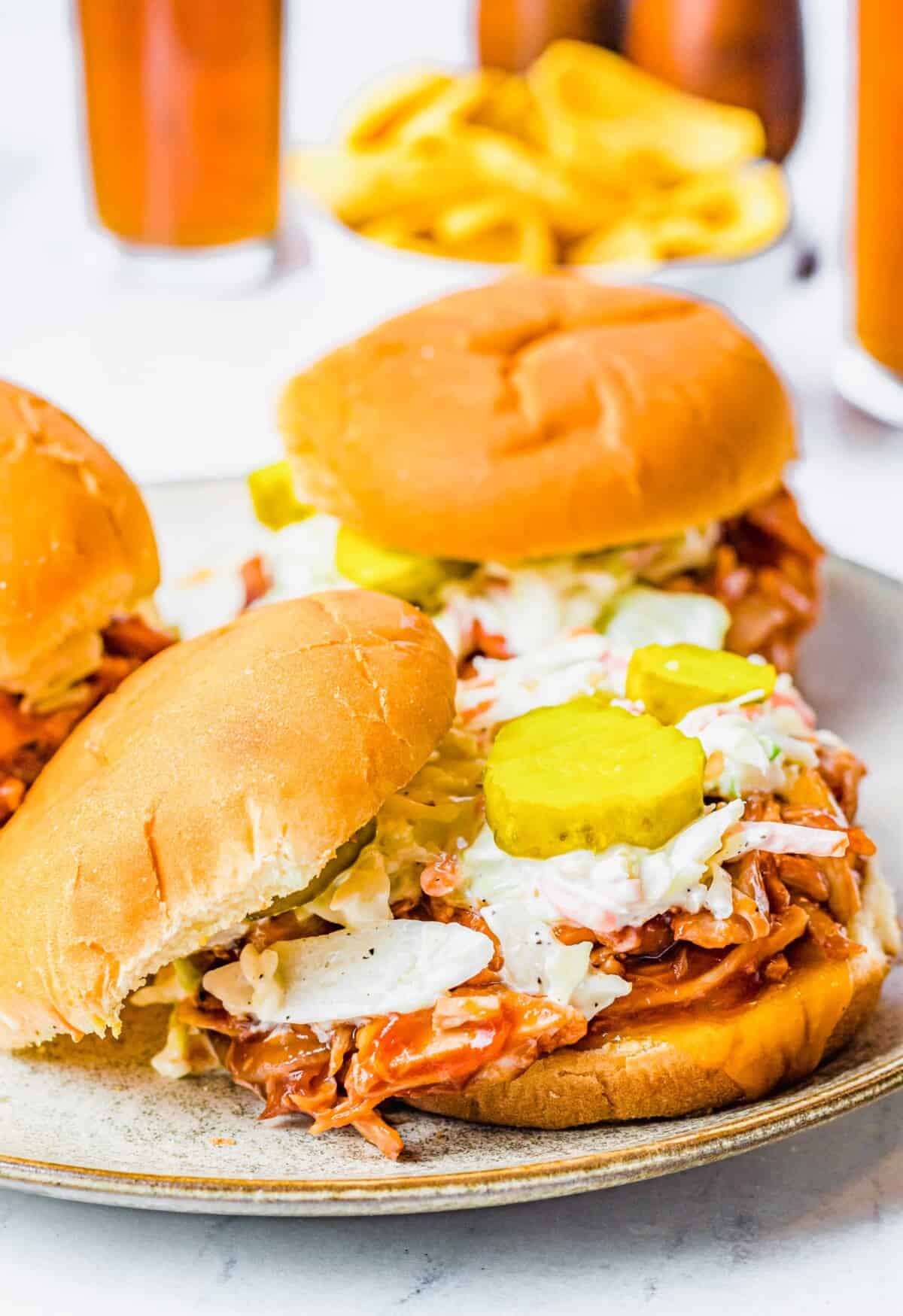 The top bun of a sandwich is put to the side to reveal pickles, coleslaw and pulled chicken.