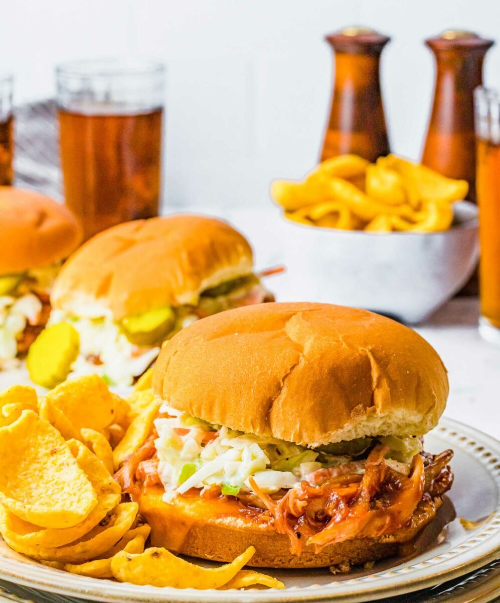 A BBQ chicken sandwich is on a plate next to some chips. 