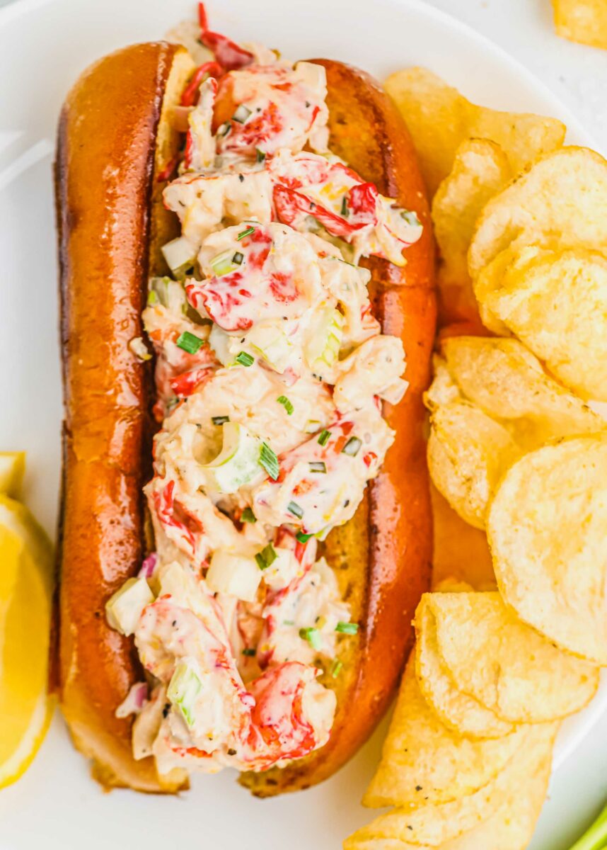 A lobster roll is placed next to a serving of chips.