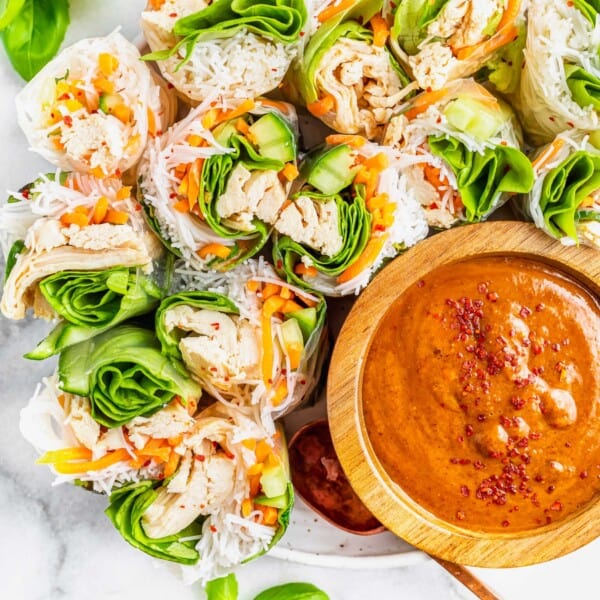 Summer rolls are halved and placed next to a wooden bowl of dipping sauce.
