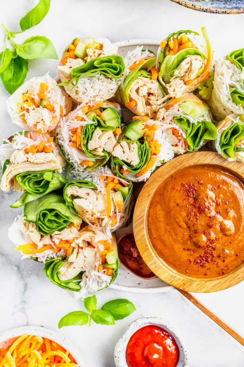 Summer rolls are halved and placed next to a wooden bowl of dipping sauce. 