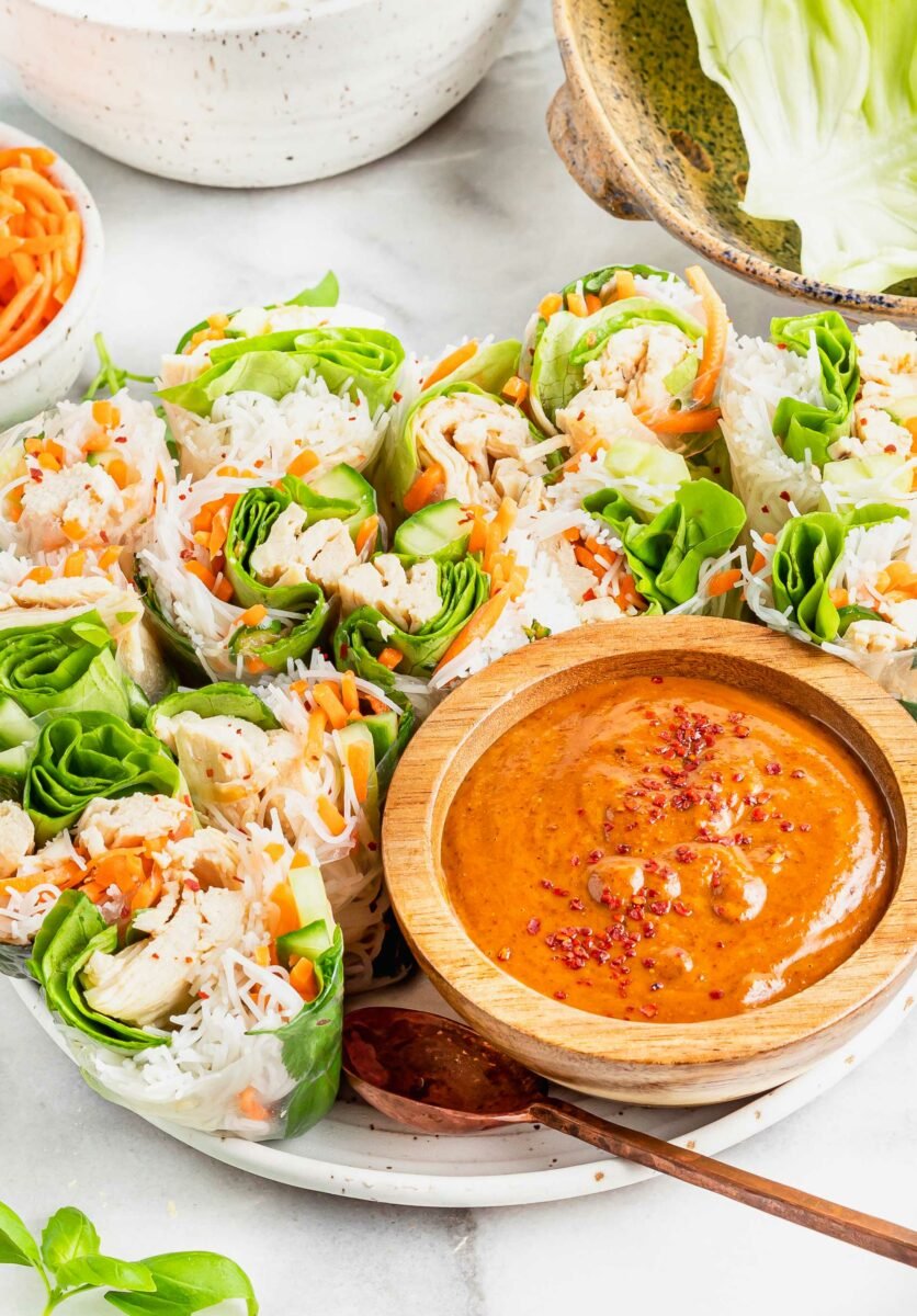 A bowl of satay sauce is placed next to chicken summer rolls. 