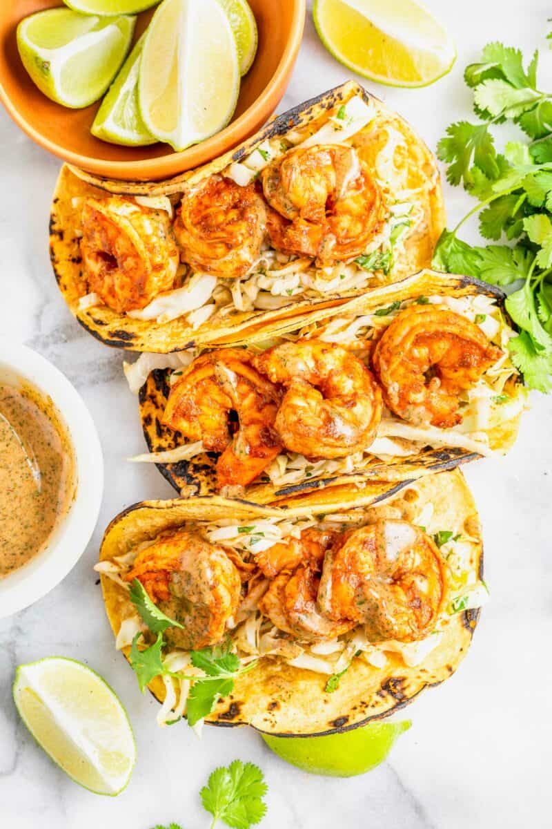 Three shrimp tacos are placed on a white surface. 