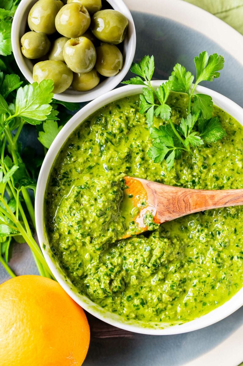 A wooden spoon is dipped into the bowl of gremolata. 