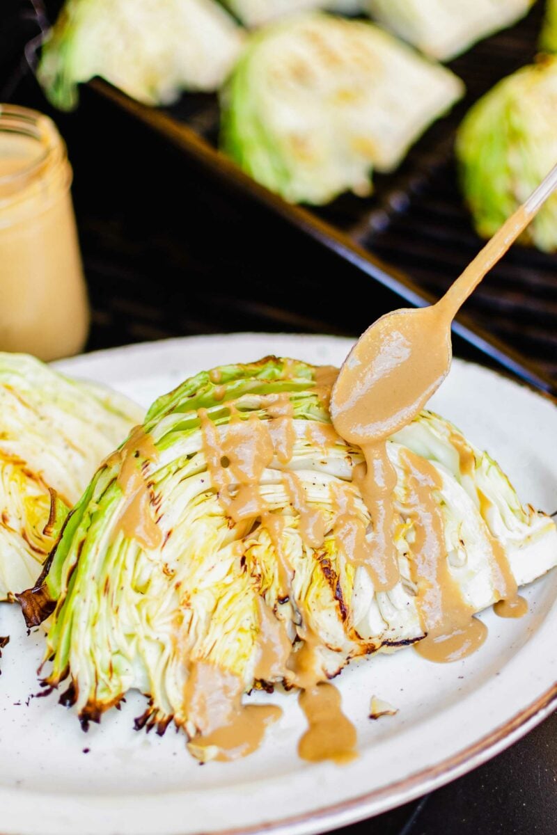 Tahini-soy sauce is being drizzled over a slice of grilled cabbage.